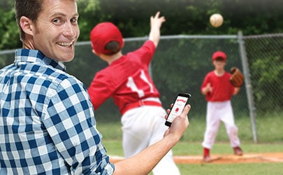 man checking his phone while watching children playing ball